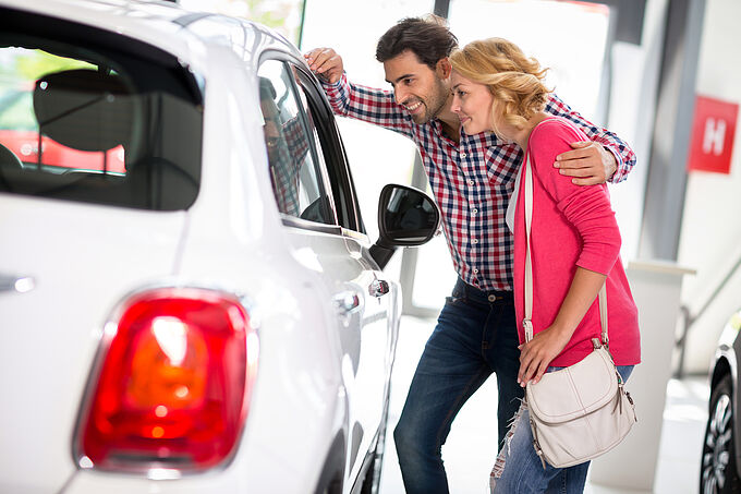 Young couple chooses to buy a car in car dealership saloon Young couple chooses to buy a car in car dealership saloon